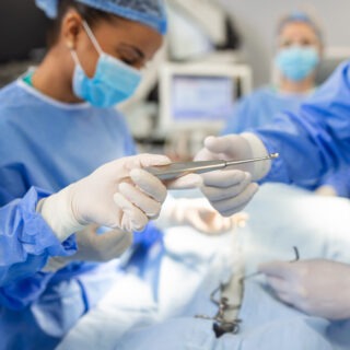 Low Angle Shot in the Operating Room, Assistant Hands out Instruments to Surgeons During Operation. Surgeons Perform Operation. Professional Medical Doctors Performing Surgery. Low Angle Shot in the Operating Room, Assistant Hands out Instruments to Surgeons During Operation. Surgeons Perform Operation. Professional Medical Doctors Performing Surgery.